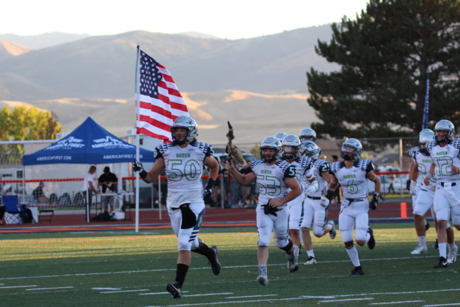 The+Ridgeline+Boys+Football+team+runs+onto+the+field+waving+the+U.S.+Flag.